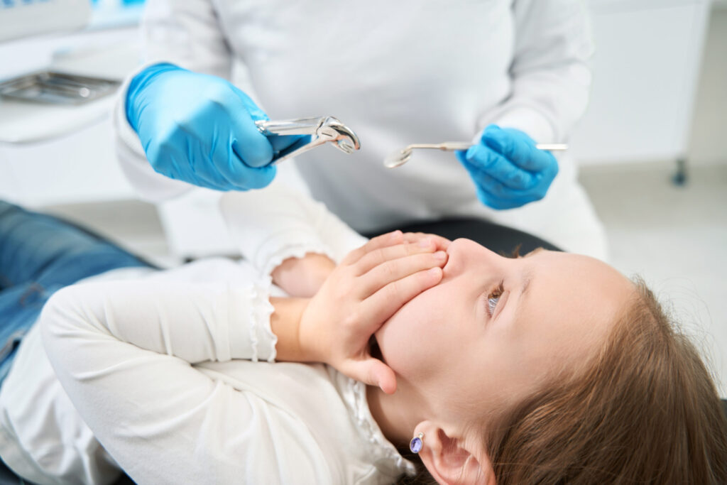 Scared child covering mouth while dentist holds tools during a pediatric dental emergency appointment